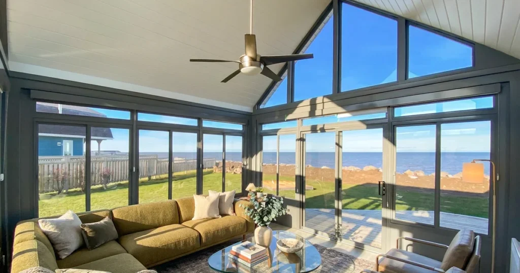 Coastal glass sunroom with large windows and a ceiling fan overlooking the water