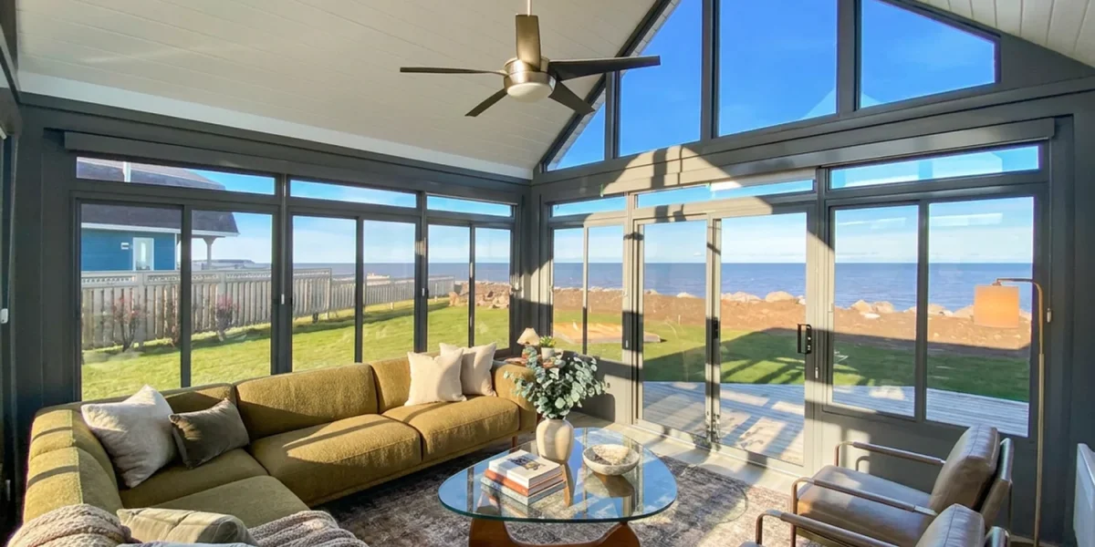 Enclosed coastal sunroom filled with warm evening light beside the water